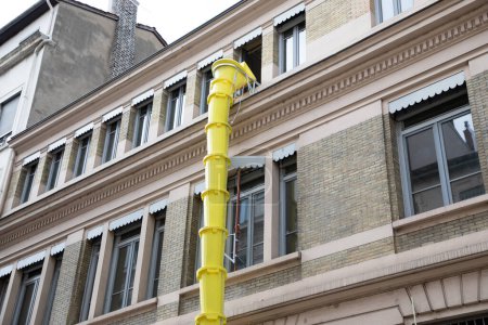 Téléchargez les photos : Glissière en plastique jaune pour l'enlèvement des débris sur le chantier de rénovation de façade de bâtiment dans la rue de la ville - en image libre de droit