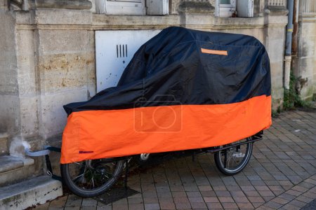 Cargo bike under a rain cover by tarpaulin plastic jacket on bicycle