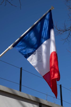 French flag on top of mast floats in the wind on blue sky