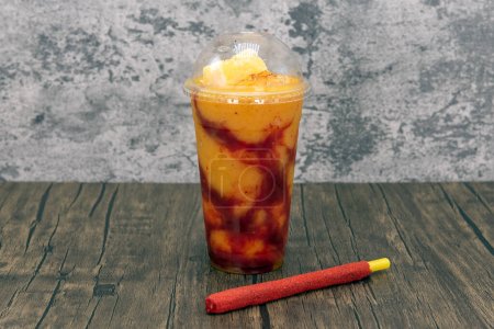 Sweet fruit flavored drink with large chunks of mango on top and sweet tamarind coated straw.