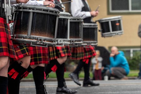 Photo for Scottish marching band drumline wearing traditional kilts and kilt hose while keeping rhythmn cadence during street parade. - Royalty Free Image