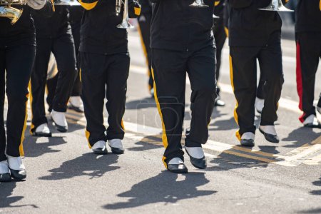 High School Marching Band, in roten Uniformen und Spucken, hält Kadenz während der Teilnahme an der lokalen Parade.