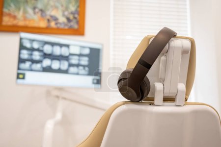 Foto de La silla dentista tiene auriculares bloqueadores de ruido para el paciente mientras revisa los rayos X de los dientes. - Imagen libre de derechos