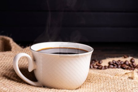 Frisch gebrühter Kaffee. Kaffeetasse oder Becher auf einem schwarzen Holztisch mit gerösteten Kaffeebohnen. Espresso Mokka Cappuccino Barista auf dunklem Hintergrund