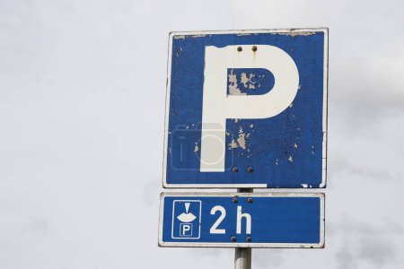 Two hours of free car parking when using a parking disc shown on a worn out road sign.