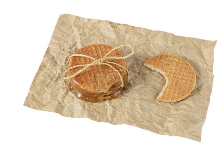 Photo for Closeup of a stack of stroopwafels on a brown paper, next to another biscuit with a bite_white background. - Royalty Free Image