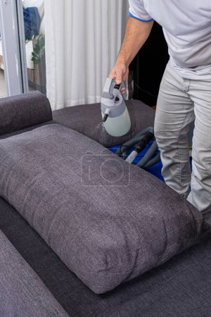 Foto de Hombre vertiendo un líquido para limpiar e impermeabilizar cojines sofá _ vertical. - Imagen libre de derechos