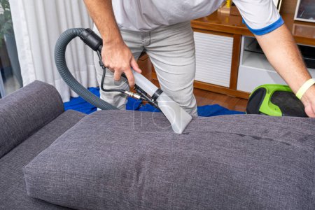 Photo for Man using a special vacuum to clean gray sofa cushions_side view. - Royalty Free Image