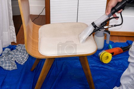 Foto de Hombre usando un vacío especial para limpiar la tapicería de la silla _ vista lateral. - Imagen libre de derechos