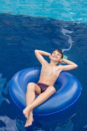 Smiling Brazilian 9 year old in the pool on a sunny day, with arms outstretched and sitting on a buoy.