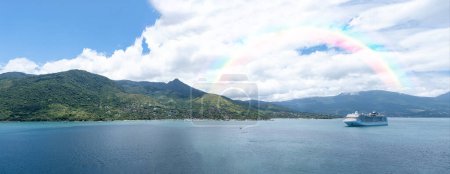 Téléchargez les photos : Panoramic photo of Ilha Bela on a sunny day with a ship anchored. In the background a rainbow. - en image libre de droit