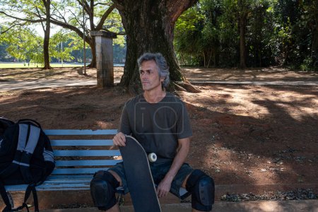 Brazilian skateboarder over 50 years old relaxing on a bench in a square_1.