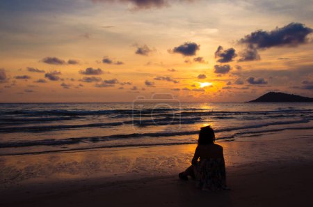 Foto de Silhouette of girl sitting on beach with sunset - Imagen libre de derechos