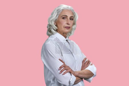 Téléchargez les photos : Portrait de dame âgée aux cheveux gris avec les bras croisés. Isolé sur fond rose. - en image libre de droit
