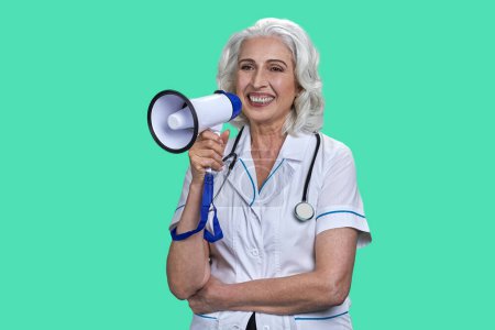 Photo for Smiling aged senior female doctor with megaphone. Happy cheerful lady with stethoscope isolated on green. - Royalty Free Image