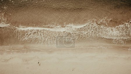 Téléchargez les photos : Mouvement lent des vagues d'eau de mer lavant la plage de sable. Vue du dessus du drone. - en image libre de droit