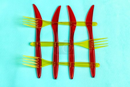 Téléchargez les photos : Couteaux jetables en plastique rouge et fourchettes jaunes. Isolé sur fond turquoise. - en image libre de droit