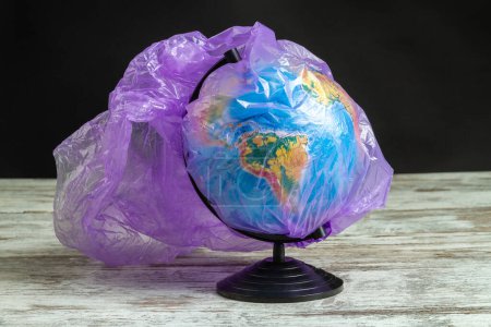 Foto de Globo de tierra cubierto con bolsa de plástico púrpura. Contaminación del medio ambiente conceptual. - Imagen libre de derechos