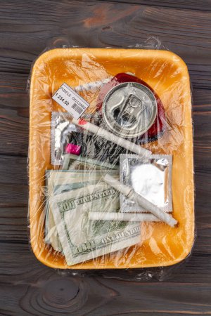 Foto de Top view cosas adolescentes envueltos en plástico. Dinero con condón y cigarrillos. - Imagen libre de derechos