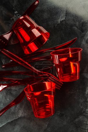 Photo pour Tasses en plastique jetables rouges avec fourchettes et couteaux. Vue verticale sur le dessus. - image libre de droit