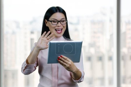 Téléchargez les photos : Young asian businesswoman to someone via tablet pc. Blurred windows backgorund. - en image libre de droit