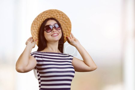 Téléchargez les photos : Portrait of happy young brunette woman wearing sunglasses and straw hat. Bright blurred background. - en image libre de droit
