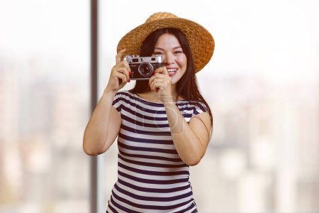 Foto de Young happy tourist asian woman in straw hat with vintage photo camera. Blurred windows background. - Imagen libre de derechos