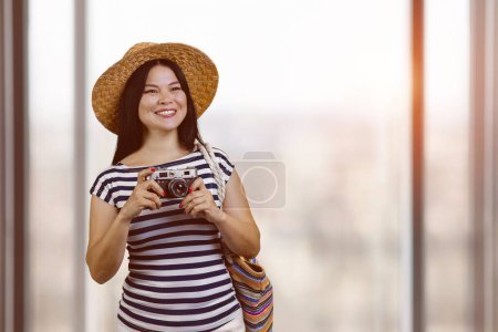 Foto de Portrait of happy asian cheerful female tourist with vintage photo camera. Indoor blurred window background. - Imagen libre de derechos