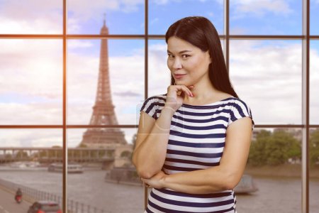 Foto de Young sexy korean casual dressed woman posing indoors. Checkered windows with view on Eiffel Tower in Paris. - Imagen libre de derechos