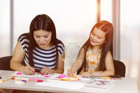 Téléchargez les photos : Brunette mother and her cute little daughter are drawing together. Mom and her girl are spending time together. Art and creativity. - en image libre de droit