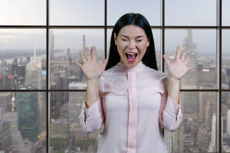 Foto de Portrait of young asian woman screaming out loud. Checkered windows and cityscape background. - Imagen libre de derechos