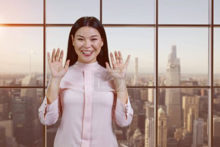 Téléchargez les photos : Portrait of young asian woman showing her hands. Checkered windows and cityscape background. - en image libre de droit