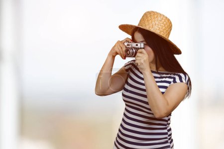 Téléchargez les photos : Young brunette woman taking a photo on vintage camera. Abstract indoor blurred background. - en image libre de droit