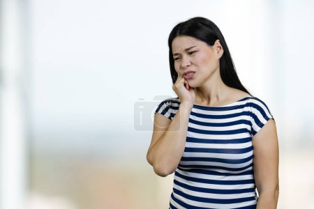 Photo for Woman suffering from toothache touching her cheek. Bright windows background. - Royalty Free Image