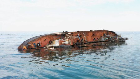 Foto de View from the drone flying closely over the broken rusty oil tanker ship. Old rusty overturned oil tanker lying on its edge in the shallow water. - Imagen libre de derechos