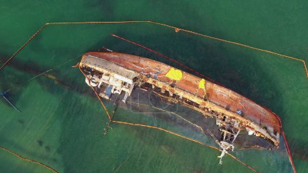 Foto de Aerial top view of overturned broken rusty oil tanker ship in the shallow water. Drowned ship after the wreck. - Imagen libre de derechos