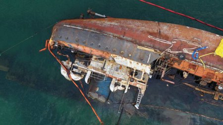 Téléchargez les photos : Aerial top view of overturned broken rusty oil tanker ship after the wreck. Drowned sunken ship in the shallow water. - en image libre de droit