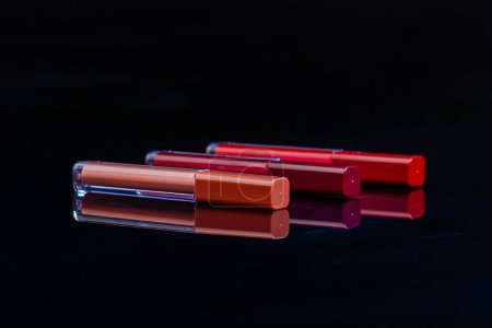 Téléchargez les photos : Three lip gloss sticks with closed caps. Reflective surface and black background. - en image libre de droit