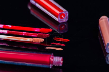 Photo for Lip gloss strokes on black reflective surface. Colored glass sticks for brushes. - Royalty Free Image