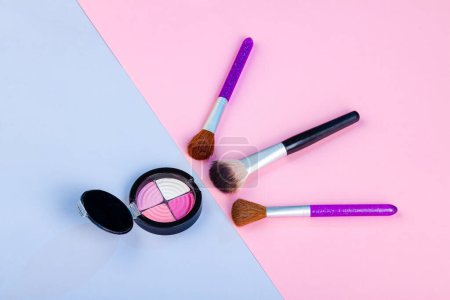 Photo for Top view of round eyeshadow palette with brushes. Blue and pink background. - Royalty Free Image