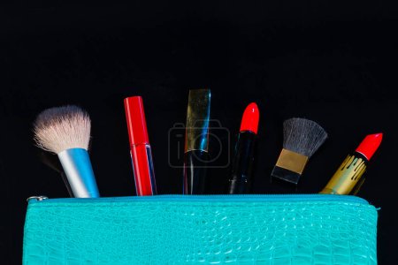 Foto de Monedero azul y herramientas de maquillaje aisladas en negro. Pinceles con lápiz labial rojo y brillo labial. - Imagen libre de derechos