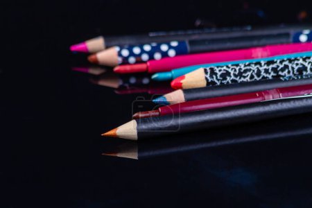 Téléchargez les photos : Gros plan ensemble de divers crayons d'eye-liner cosmétiques de couleur. Surface réfléchissante sombre. - en image libre de droit