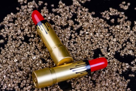 Téléchargez les photos : Deux rouges à lèvres rouges et de minuscules rochers dorés. Gros plan outils de maquillage cosmétique. - en image libre de droit