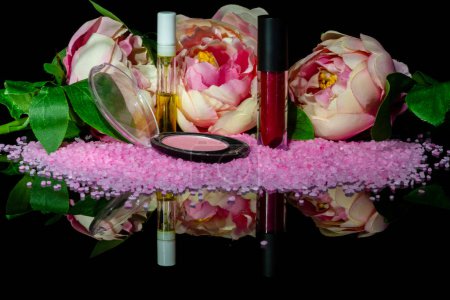 Foto de Still life make up accessories and flowers on reflective surface. Isolated on black. - Imagen libre de derechos