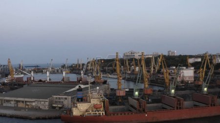 Téléchargez les photos : Warehouse and tower cranes on a sea port in the evening. Industrial scape at twilight sky. - en image libre de droit