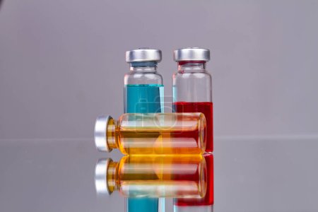 Foto de Colección de frascos de vidrio con medicamentos coloreados. Superficie reflectante con fondo gris. - Imagen libre de derechos