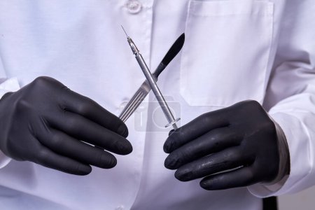 Téléchargez les photos : Le médecin chirurgien tient un scalpel avec une seringue. Instrument de concept chirurgical. - en image libre de droit