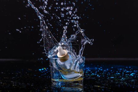 Foto de Frasco de perfume que cae en una taza de vidrio con salpicaduras de agua. Aislado sobre fondo negro. - Imagen libre de derechos