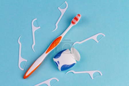 Téléchargez les photos : Brosse à dents avec pinces à soie dentaire et fil. Vue du dessus fond bleu. - en image libre de droit