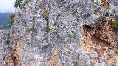 Téléchargez les photos : Falaise rocheuse au-dessus de la vallée boisée et route de campagne. Vue aérienne des falaises escarpées des montagnes. Village de montagne à distance. - en image libre de droit